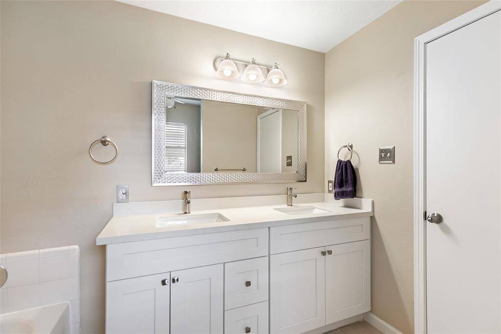Another view of the primary bathroom showing the double vanity with sleek faucets and a large, framed mirror.