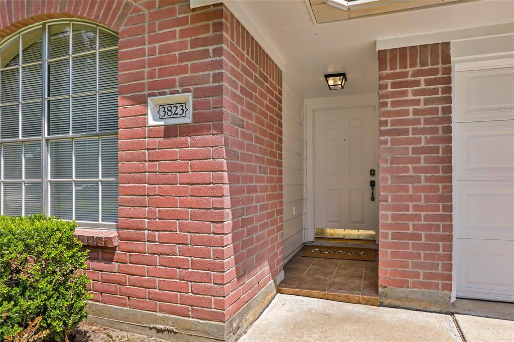 This photo showcases a welcoming entryway with a classic brick exterior and arched window. The front door is sheltered under a small porch, and a house number is prominently displayed.