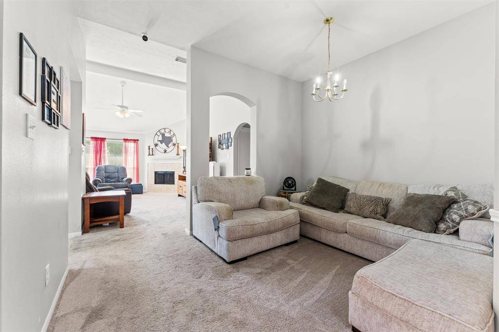 Cozy living area with soft neutral-toned sofas and carpet, leading to a bright room with red curtains and a fireplace. The space features a chandelier, archway, and ceiling fan, creating a welcoming atmosphere.  (sofa not included)