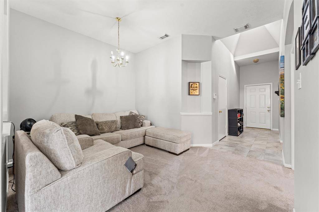 Bright and spacious living area featuring soft carpet, a cozy sectional sofa, and a chandelier. The room opens up to a tiled hallway leading to a front door, offering a welcoming entrance.  (sofa not included)
