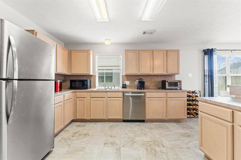 Bright, spacious kitchen with light wood cabinetry, stainless steel appliances, and ample counter space. Large windows provide plenty of natural light.