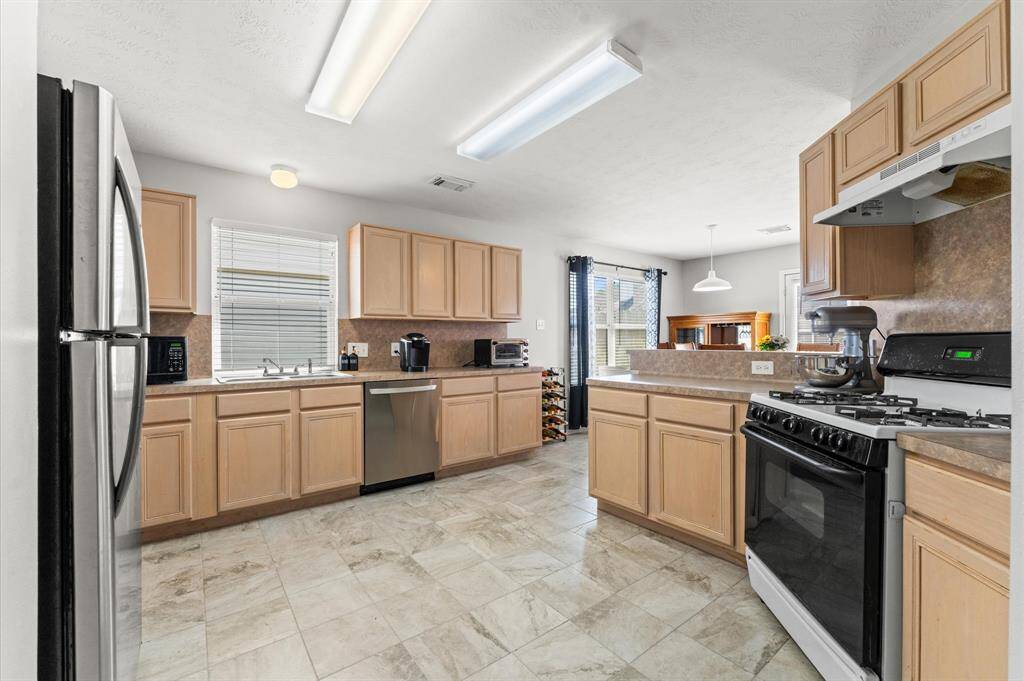 Bright and spacious kitchen featuring light wood cabinets, stainless steel appliances, and tiled flooring. A gas stove and ample counter space make it ideal for cooking. The kitchen opens to a dining area with large windows, providing natural light.