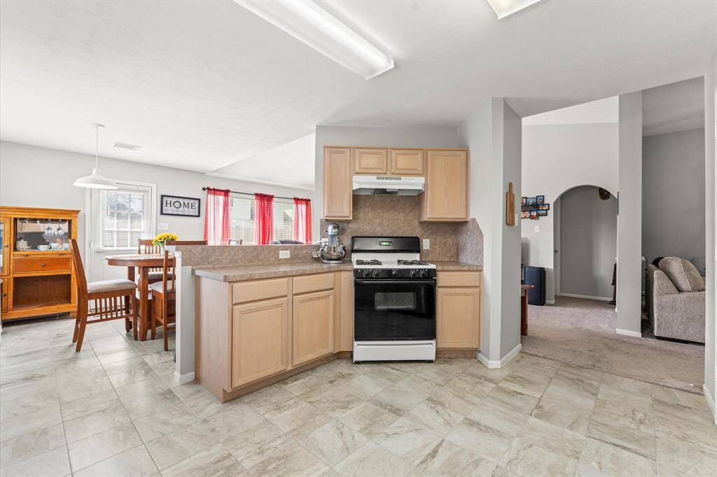 This inviting kitchen features light wood cabinets, a gas stove, and a cozy dining area with natural light from large windows. The open layout seamlessly connects to a comfortable living space, offering a perfect setting for family gatherings.
