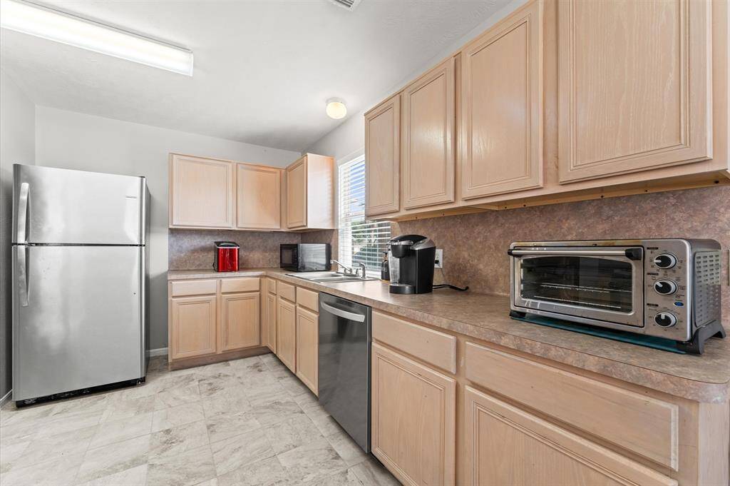 Modern kitchen with light wood cabinets, stainless steel appliances, and ample counter space. Includes a brand new dishwasher. Bright and functional layout.
