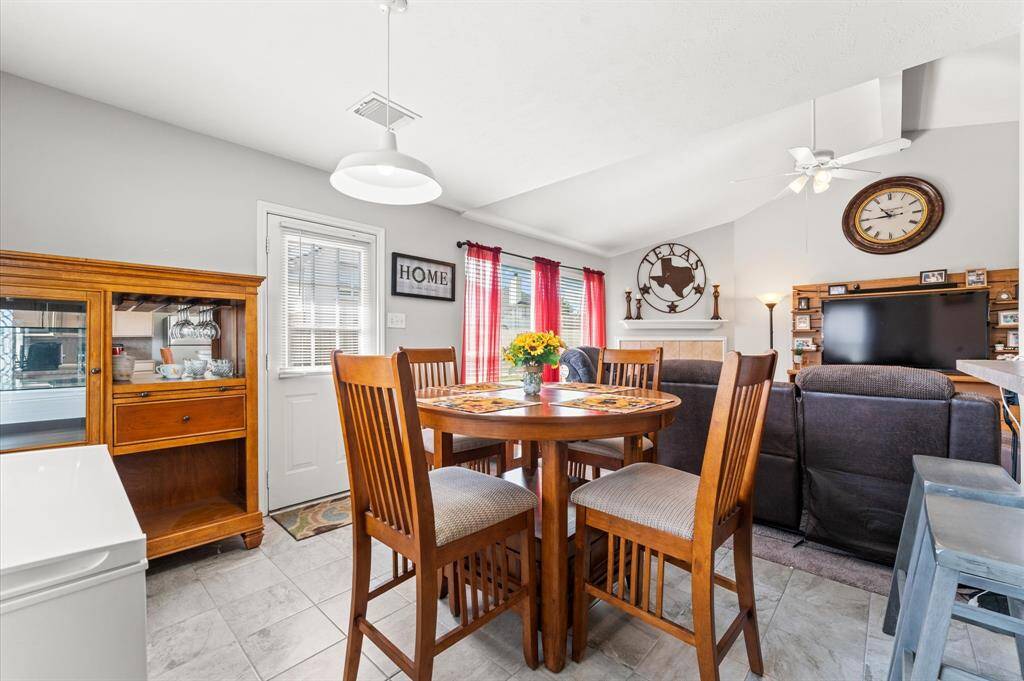 This inviting living space features a cozy dining area,  a comfortable seating area ., The room is brightened by natural light from large windows, has a high ceiling with a ceiling fan.