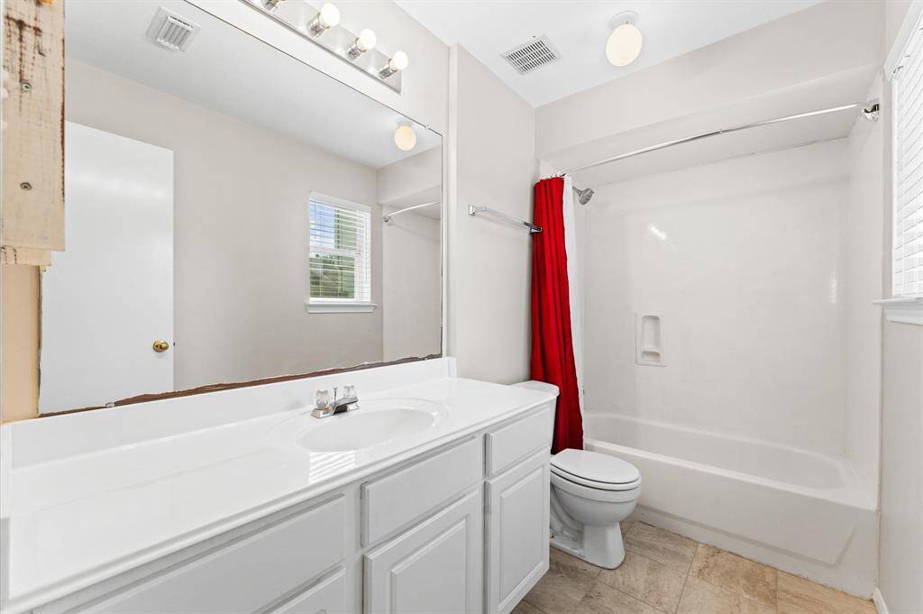 Bright bathroom with a large mirror, white vanity, and bathtub. It features tile flooring, and a window for natural light.
