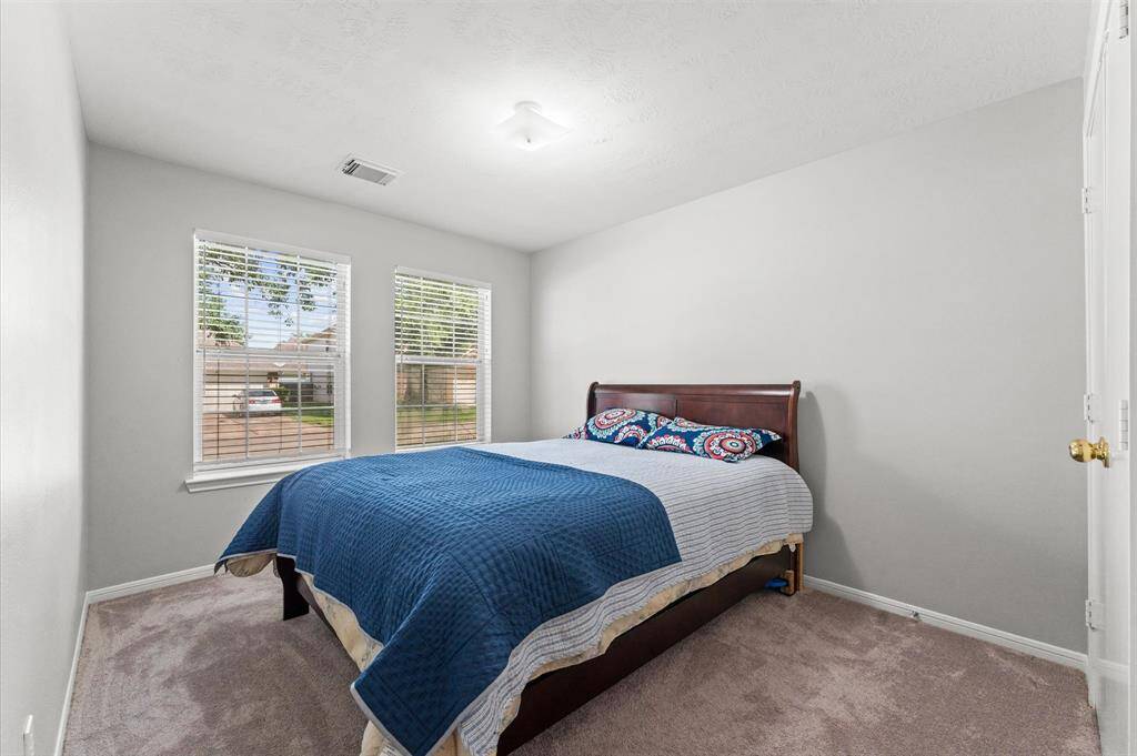 This cozy bedroom features soft carpeting, neutral walls, and ample natural light from two windows. The room creates a welcoming atmosphere.