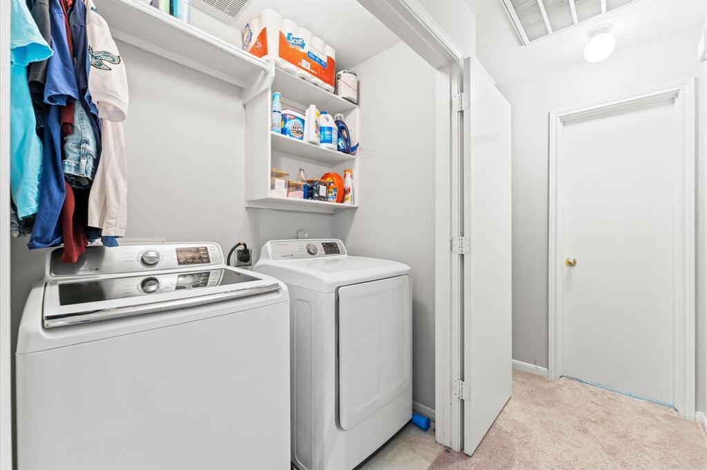 This photo shows a compact laundry area. It includes shelving for storage and a hanging rod for clothes. The space is well-lit and has easy access with adjacent doors.