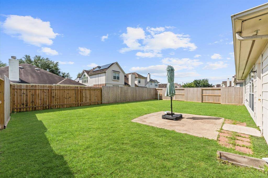 Spacious backyard with well-maintained lawn, surrounded by a wooden fence for privacy. There's a concrete patio area, ideal for outdoor furniture or a barbecue setup. Perfect for family gatherings or relaxation.