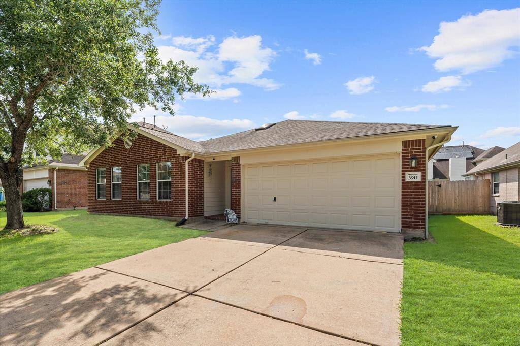 This photo shows a charming single-story brick home with a two-car garage. It features a well-maintained front yard with a tree, and a concrete driveway leading to the garage. The house has a welcoming appearance with multiple front windows and a neatly trimmed lawn.