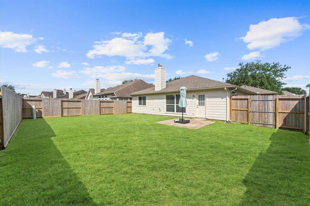 This photo showcases a spacious, fenced backyard with a well-maintained lawn, perfect for outdoor activities. The house features a light exterior with a patio area, ideal for relaxing or entertaining.  New fence August 2024.
