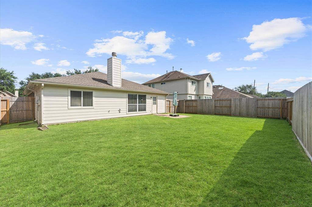 Spacious backyard with well-maintained lawn, surrounded by a wooden fence. The house features a chimney and large windows, offering a bright and open feel. Ideal for outdoor activities and privacy.  New fence August 2024.