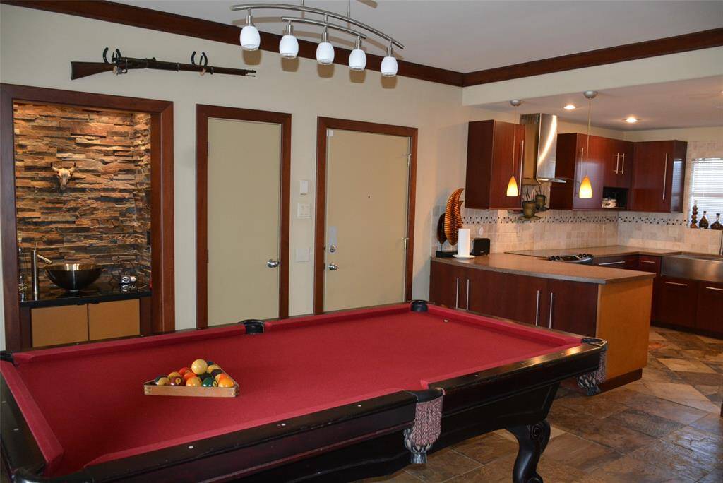 Step into a versatile space featuring a formal dining area, currently showcasing a pool table, with a sleek modern kitchen just steps away. Enjoy the convenience of a stylish wet bar and easy access through the nearby main entrance.