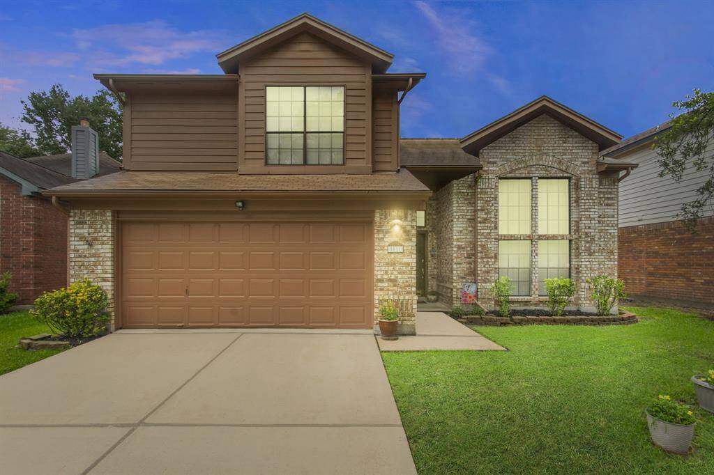 This charming two-story home features a brick and wood exterior with a spacious garage. The manicured front lawn and well-maintained garden add curb appeal, while large windows bring in natural light. Perfect for families seeking a welcoming and cozy atmosphere.