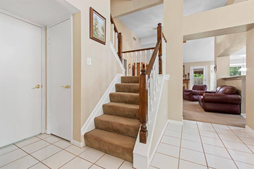This photo showcases an inviting entryway with a carpeted staircase featuring wooden railings. The area is bright and connects to a cozy living space.