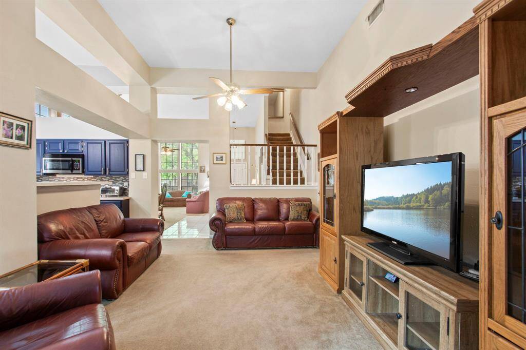 This spacious living room features high ceilings, a cozy carpeted floor, and large windows for natural light. It provides easy access to the kitchen with modern appliances. A staircase leads to the upper level, enhancing the open feel.