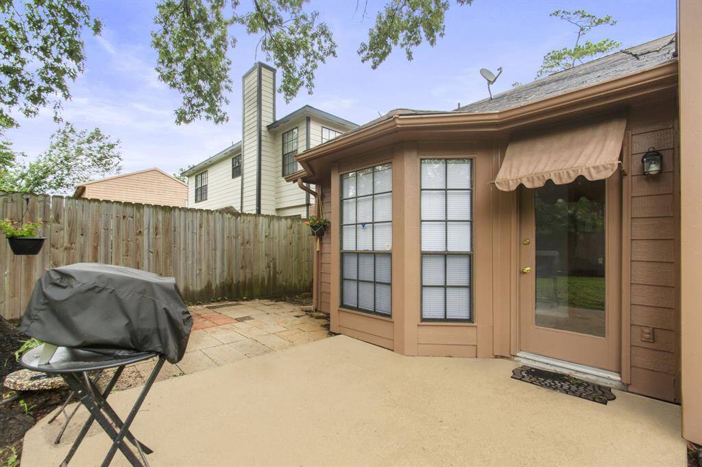 This photo shows a cozy backyard patio with a concrete surface, bordered by a wooden fence for privacy. It features a charming bay window, perfect for outdoor relaxation.