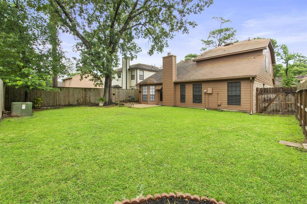 This photo showcases a spacious backyard with well-maintained grass, bordered by a wooden fence for privacy. The house features a brick and wood exterior, with large windows and a chimney, providing a cozy and inviting atmosphere. Ideal for outdoor activities and entertaining.