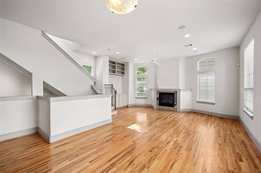 This is a modern, multi-story townhouse with a two-car garage. It features a combination of light siding and brick accents, complemented by large windows and decorative shutters. The property is surrounded by small trees and landscaping, creating a welcoming exterior.
