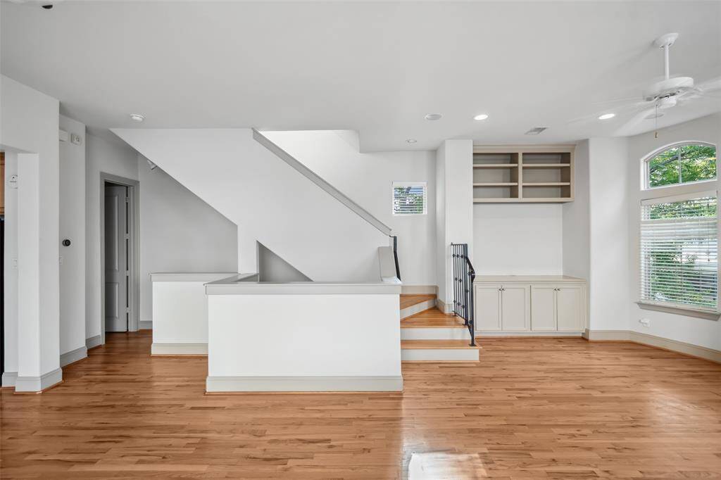 This bright, open-concept living area features hardwood floors, a modern staircase, built-in shelving, and large windows for natural light.