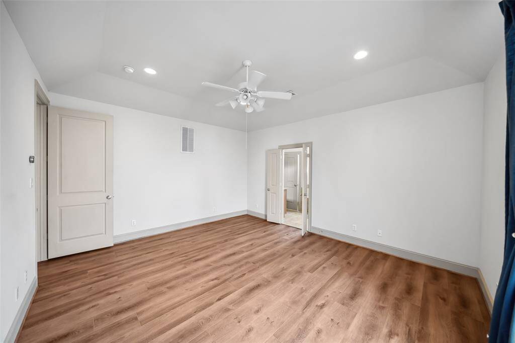 Spacious room with wood flooring, neutral walls, and a ceiling fan. Features recessed lighting, dual doors leading to an adjacent area, and ample natural light from a window with curtains.