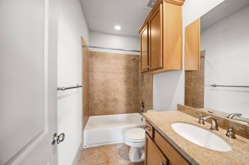 This bathroom features a clean, modern design with a granite countertop, wooden cabinetry, and a shower-tub combination with a white curtain. Natural light filters in, enhancing the space.