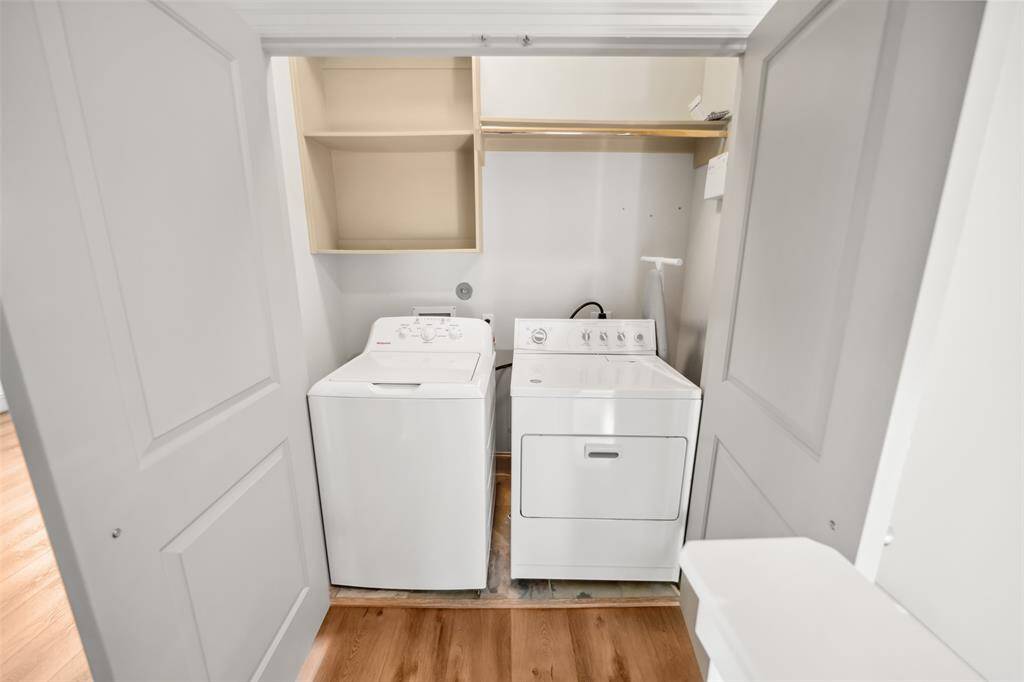 Compact laundry area with washer and dryer, featuring open shelving for storage. Light wood flooring adds warmth and brightness.