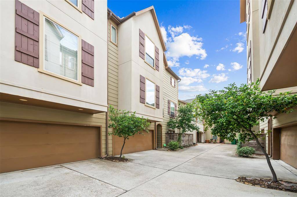 Modern townhouses with three stories and attached garages, featuring a clean, shared driveway and small trees for a touch of greenery.