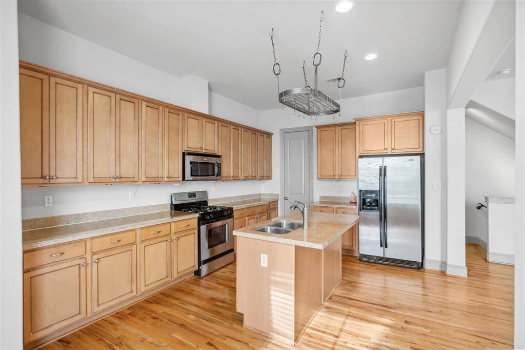 This photo showcases a bright, open-concept dining and kitchen area. It features hardwood floors, a large window with blinds, and a modern dining set. The kitchen includes wooden cabinets, a stainless steel refrigerator, and a breakfast bar with seating, creating a welcoming and functional space.