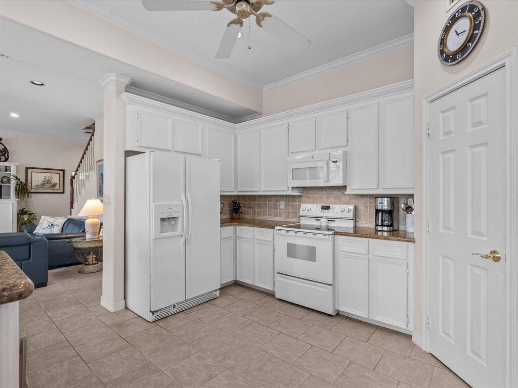 The kitchen features crisp white cabinetry providing ample storage, complemented by granite countertops, large pantry, and a tiled backsplash.