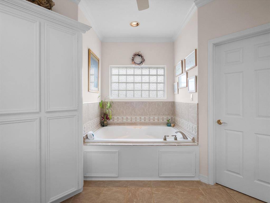 The en-suite bathroom features a deep soaking tub, perfect for relaxation, with a tiled surround and a privacy glass block window for natural light.