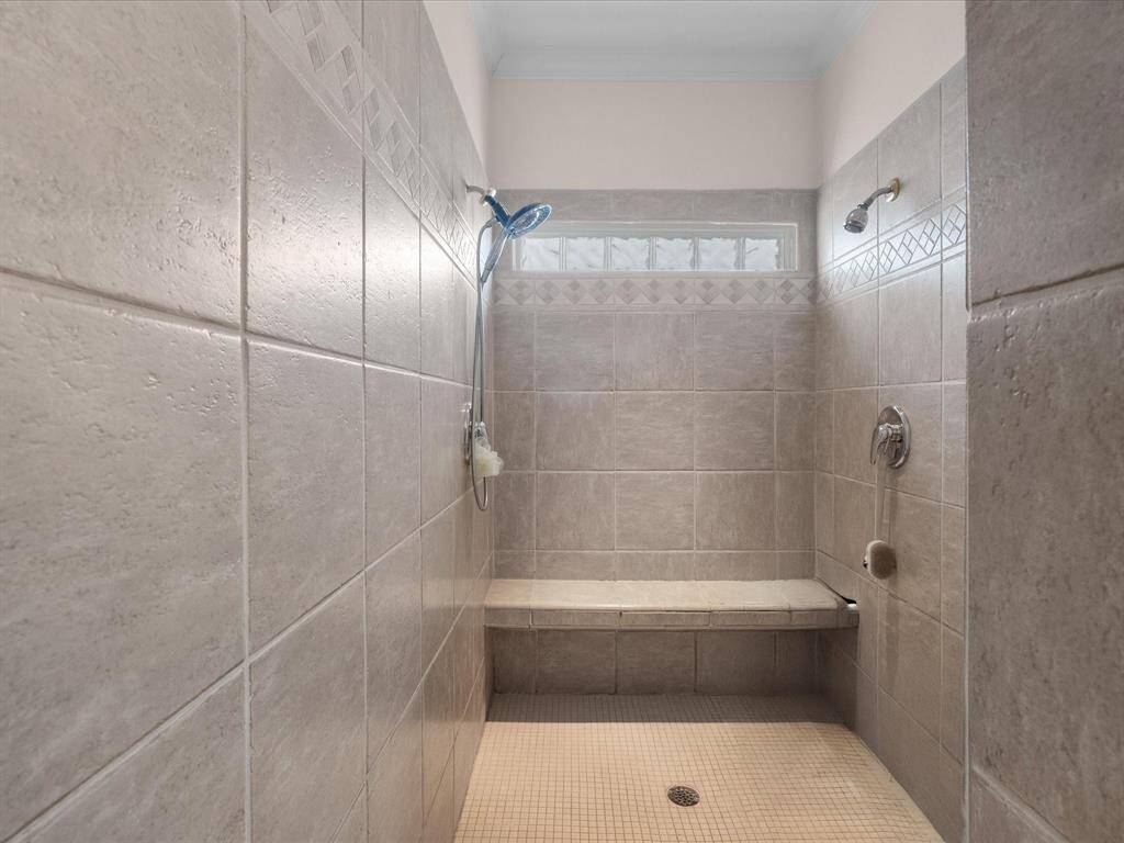 The enormous walk-in shower is fully tiled and features a built-in bench and dual showerheads. A privacy glass block window allows for natural light while maintaining seclusion