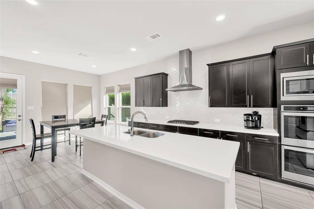 This kitchen boasts double ovens and a gas cooktop with an overhead vent, seamlessly flowing into the dining room and breakfast nook