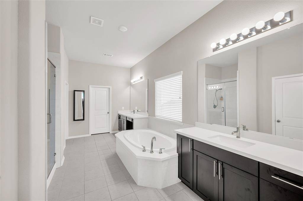 The primary bath showcases dual vanities, an oversized tub with spa features, and a spacious walk-in shower. Beyond, a generous walk-in closet seamlessly connects to the utility room, providing convenient access for laundry.