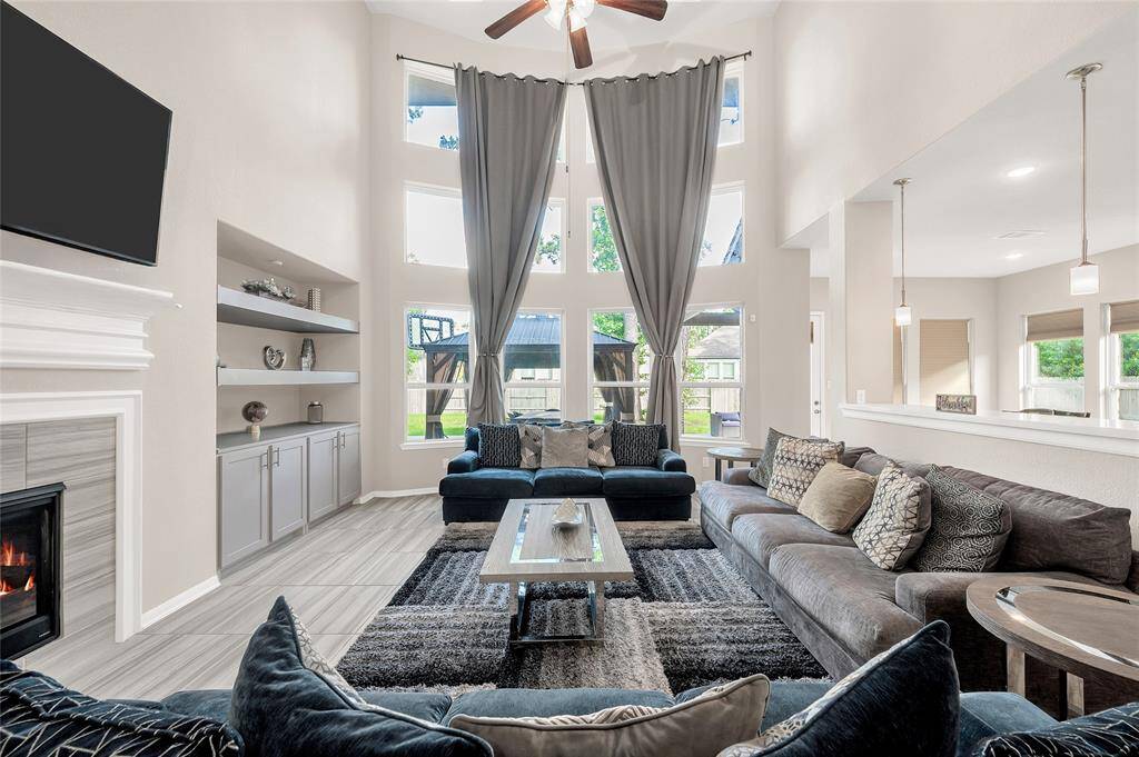 The living room’s soaring two-story ceiling beautifully showcases floor-to-ceiling windows that flood the space with abundant natural light