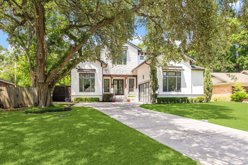 This modern two-story home features a sleek exterior with large windows, a spacious driveway, and a well-maintained lawn surrounded by mature oak trees, offering a blend of style and tranquility.