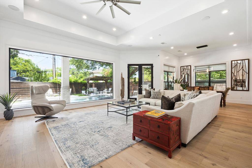 Another view of the open concept family room, offering abundant natural light and views of a lush backyard with a pool. The open layout includes elegant hardwood floors, modern furnishings, and a cozy seating area, creating a perfect space for relaxation and entertaining.