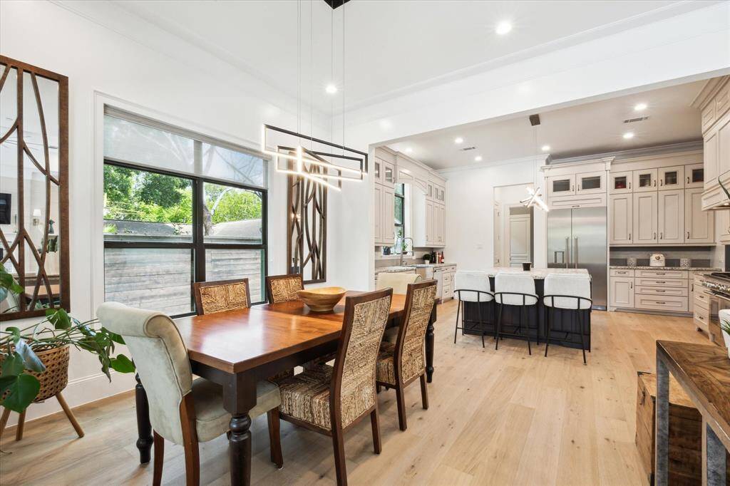 This photo showcases a bright, open-concept breakfast area and kitchen with modern lighting, hardwood floors, and large windows.