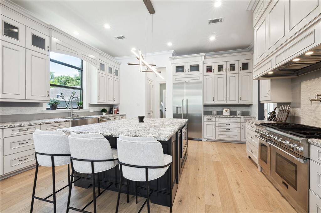 This kitchen boasts a modern design with white European double stacked, full overlay and glazed wood cabinetry with soft close doors and drawers, a large island with seating, Thermador stainless steel appliances, and ample natural light. The open layout and elegant finishes create a welcoming space ideal for cooking and entertaining.