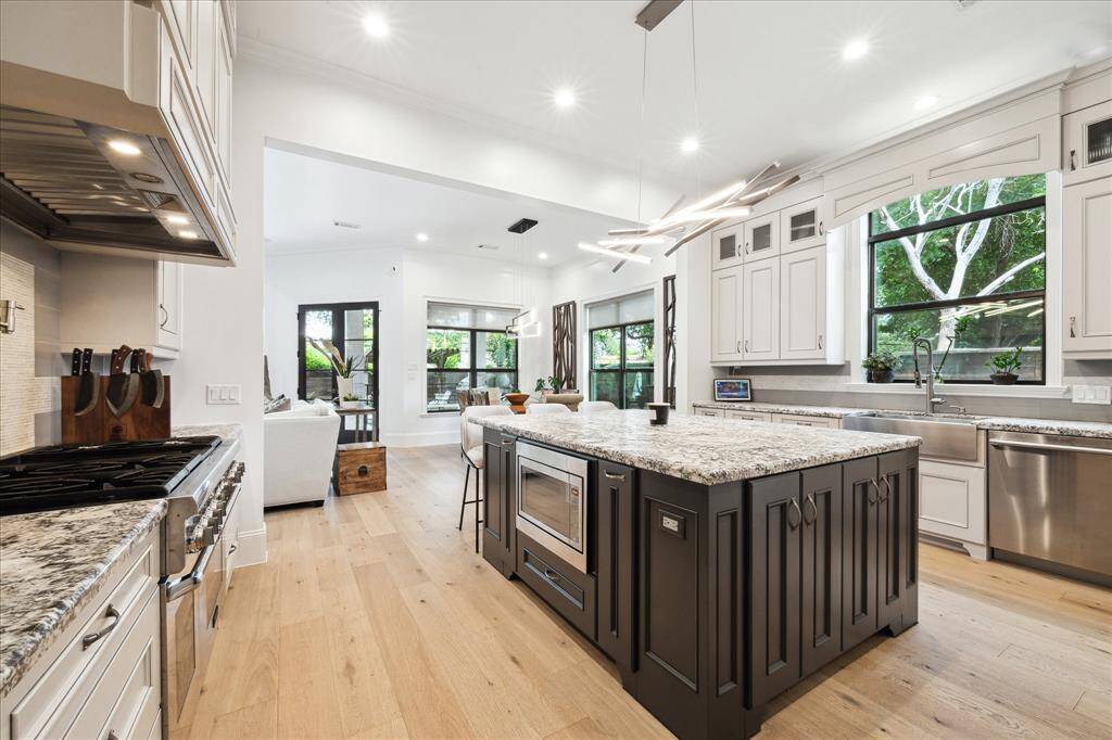 This modern kitchen features a spacious layout with a large satin finish granite island, high-end Thermador stainless steel appliances, and granite countertops. It has ample natural light, hardwood floors, and opens into the living area with large windows overlooking the amazing backyard.