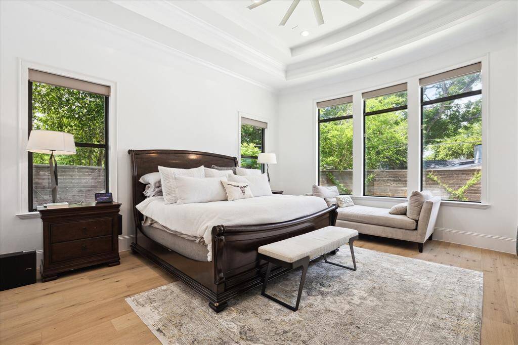 This spacious, bright primary bedroom features large windows with serene garden views, a stylish double  tray ceiling with extensive molding, and elegant hardwood floors. There is a private door leading to the rear patio and recessed lighting.
