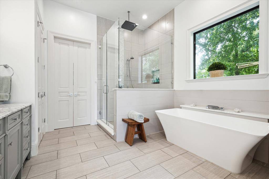 This modern bathroom features a spacious glass-enclosed shower, a sleek freestanding bathtub, and a large window for natural light. The porcelain floors and walls add a touch of elegance.