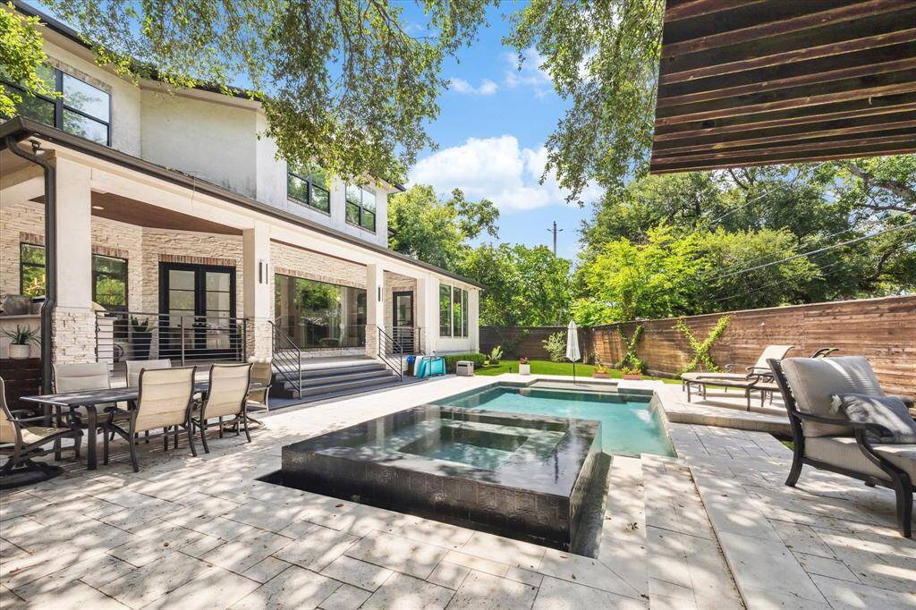 Modern backyard with a spacious patio featuring a luxurious pool and hot tub. The area includes comfortable seating and a dining set, surrounded by lush greenery and a wooden privacy fence and lots of extra green space. Perfect for entertaining and relaxation.