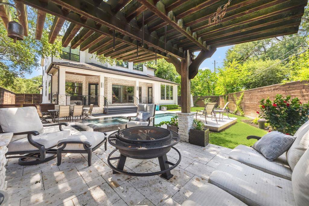 This inviting backyard features a spacious patio with comfortable seating under a pergola, a cozy fire pit, and a refreshing pool. The area is beautifully landscaped with lush greenery, providing a serene outdoor retreat perfect for relaxation and entertaining.