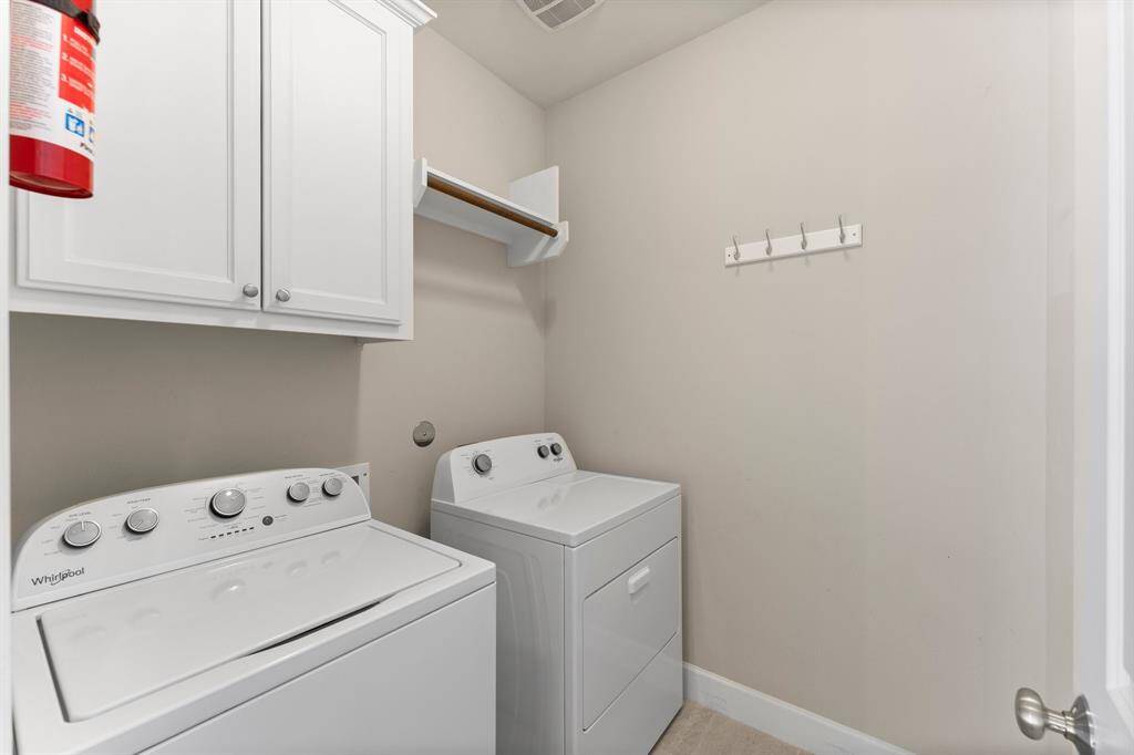This dedicated laundry room features upper cabinetry for storage, and a convenient hanging rod.