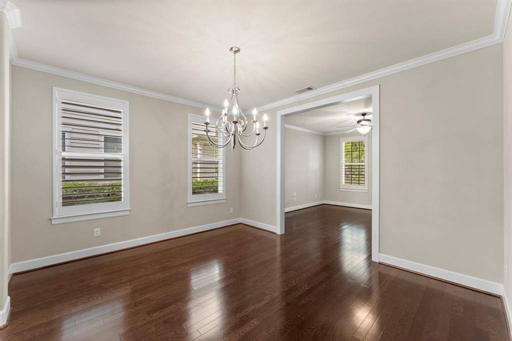 This elegant dining room features crown molding, hardwood floors, and a modern chandelier with natural light streaming through plantation shutters.