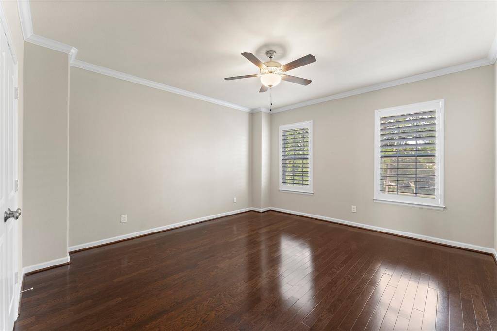 Spacious primary bedroom features rich hardwood floors, crown molding, and abundant natural light through plantation-shuttered windows.