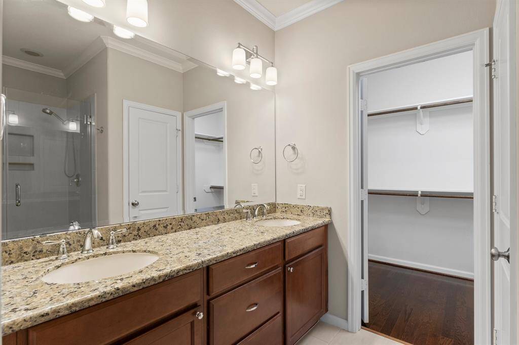 The primary bathroom features dual sinks with granite countertops, a glass-enclosed shower, and direct access to a spacious walk-in closet.