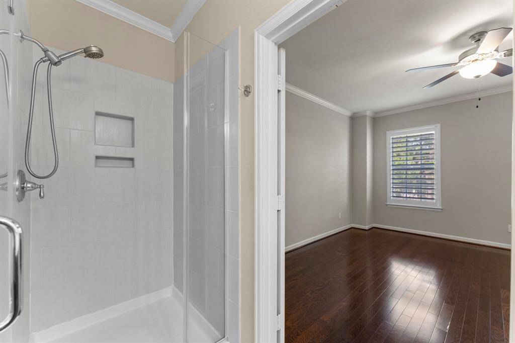 This view highlights a sleek, tiled walk-in shower and a spacious adjacent bedroom with wood flooring and natural light.