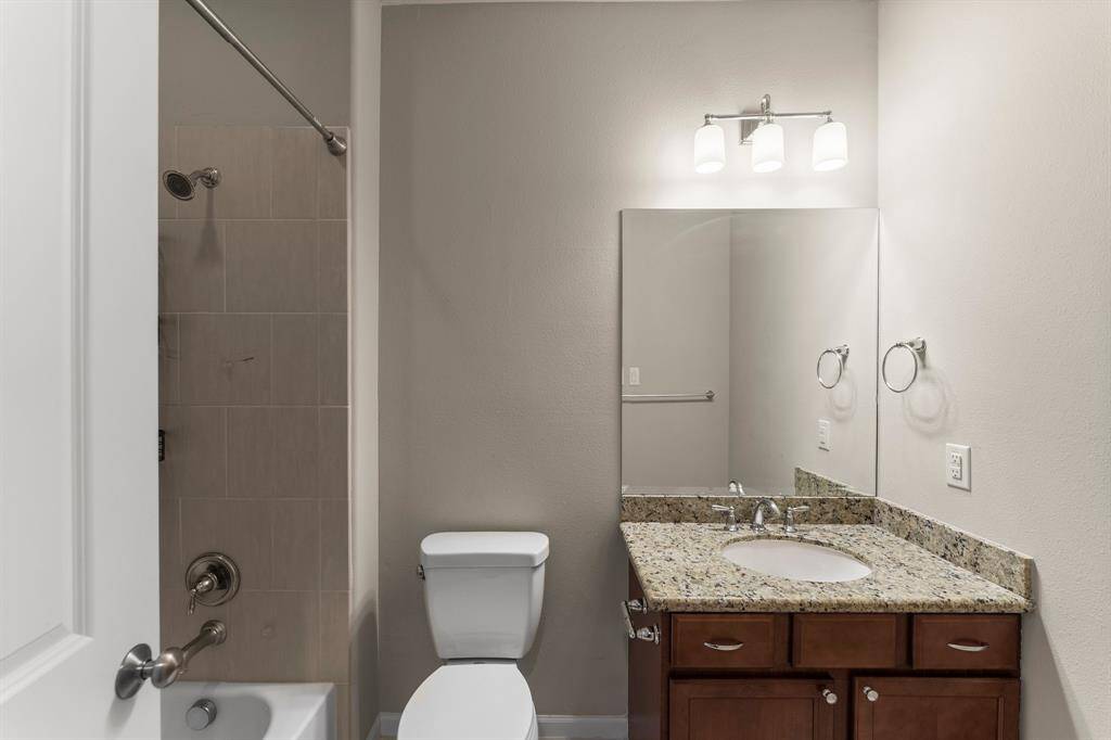 Full bathroom includes a granite vanity, rich wood cabinetry, and a tub/shower combo with neutral tile surround.